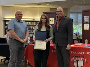 A woman holds a certificate flanked by two men.