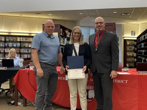 A woman holds a certificate flanked by two men.