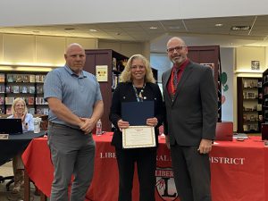 A woman holds a certificate flanked by two men.