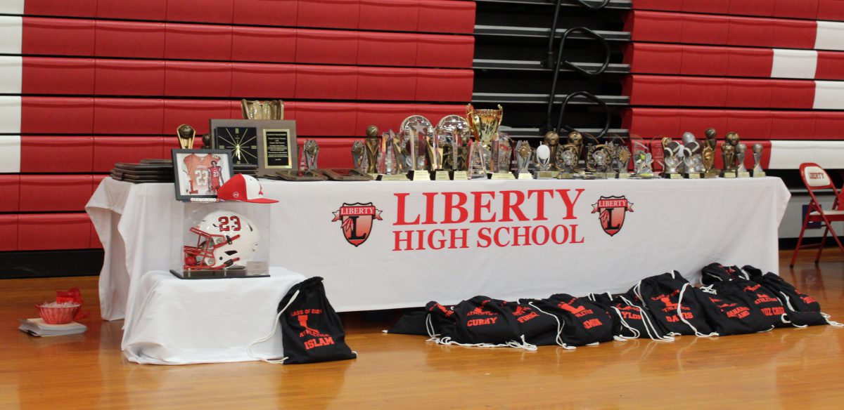 A table with a Liberty High School tablecloth is covered with awards