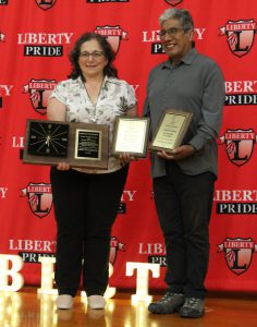 Two people hold plaques and a clock in front of a Liberty backdrop