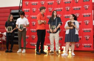 Five students, four holding plaques, stand in tront of the Liberty backdrop.
