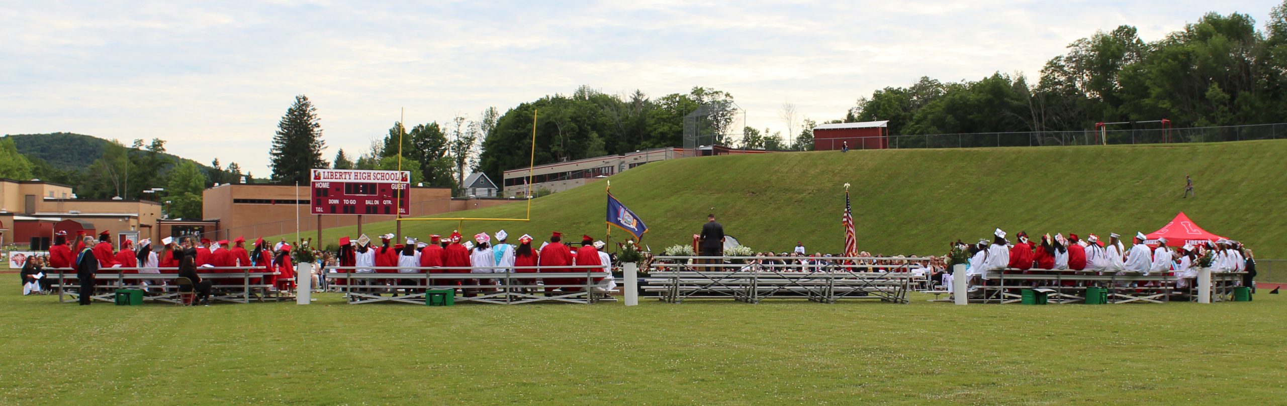 Graduates sit on bleachers, as seen from the back.