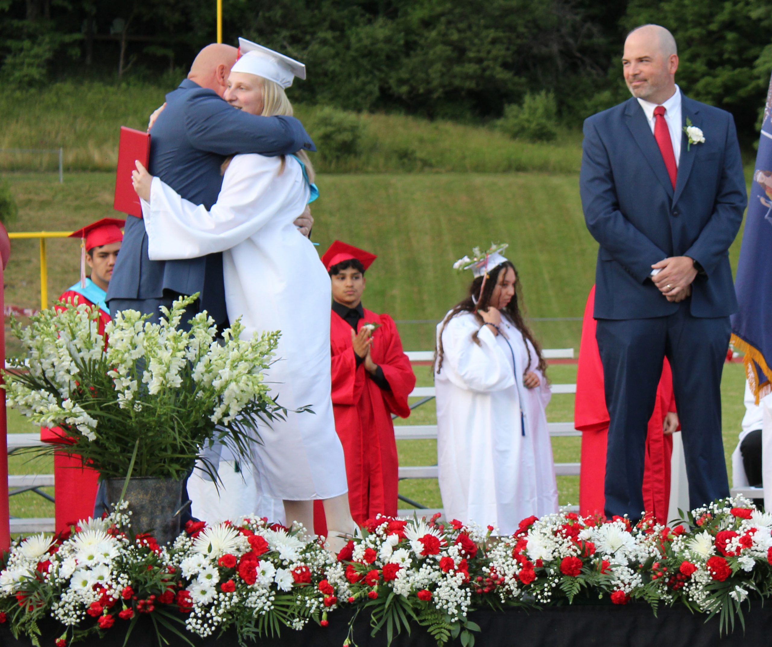 A graduate hugs an adult after she receives her diploma as a man watches