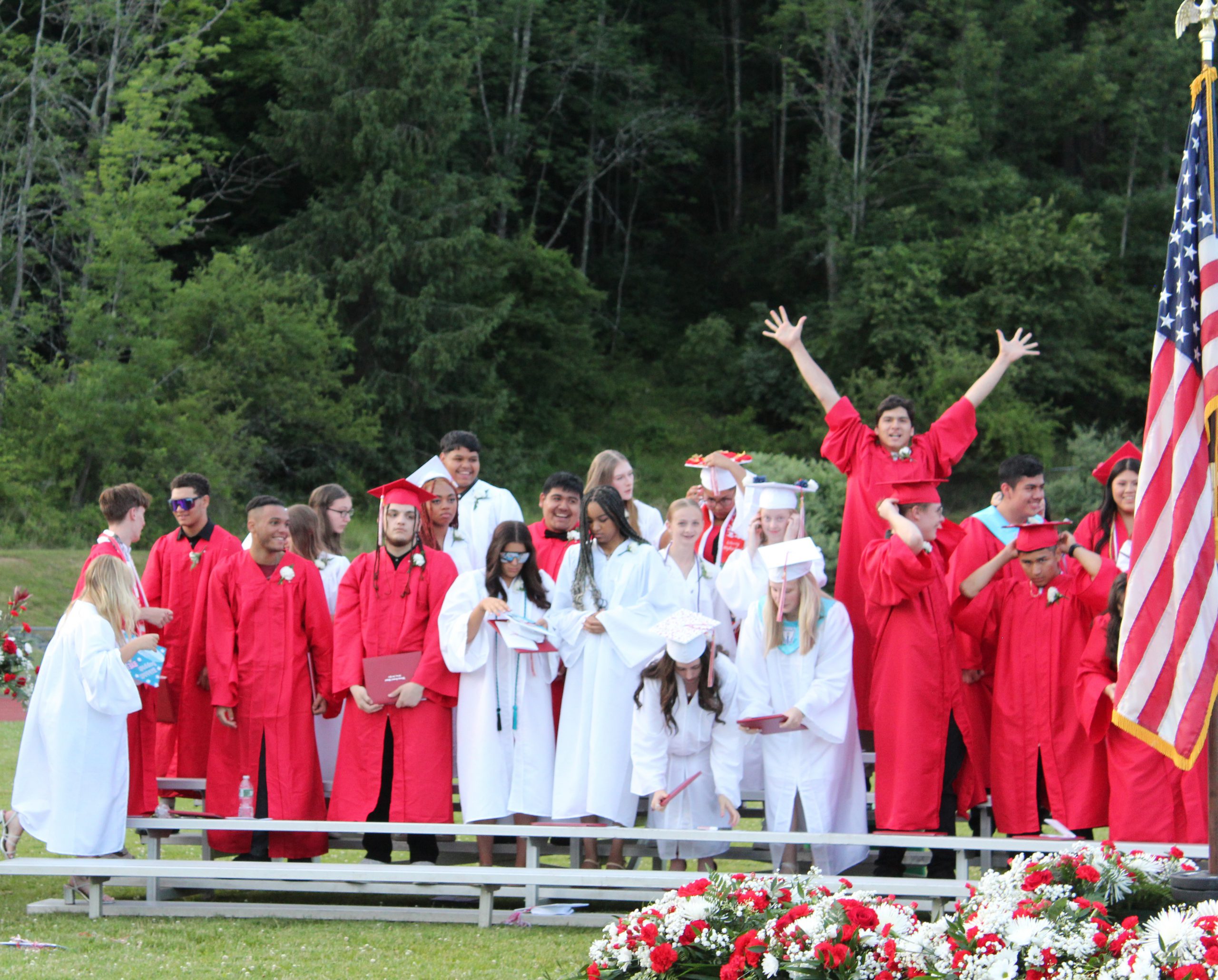 A student raises his hands in the air as other graduates stand