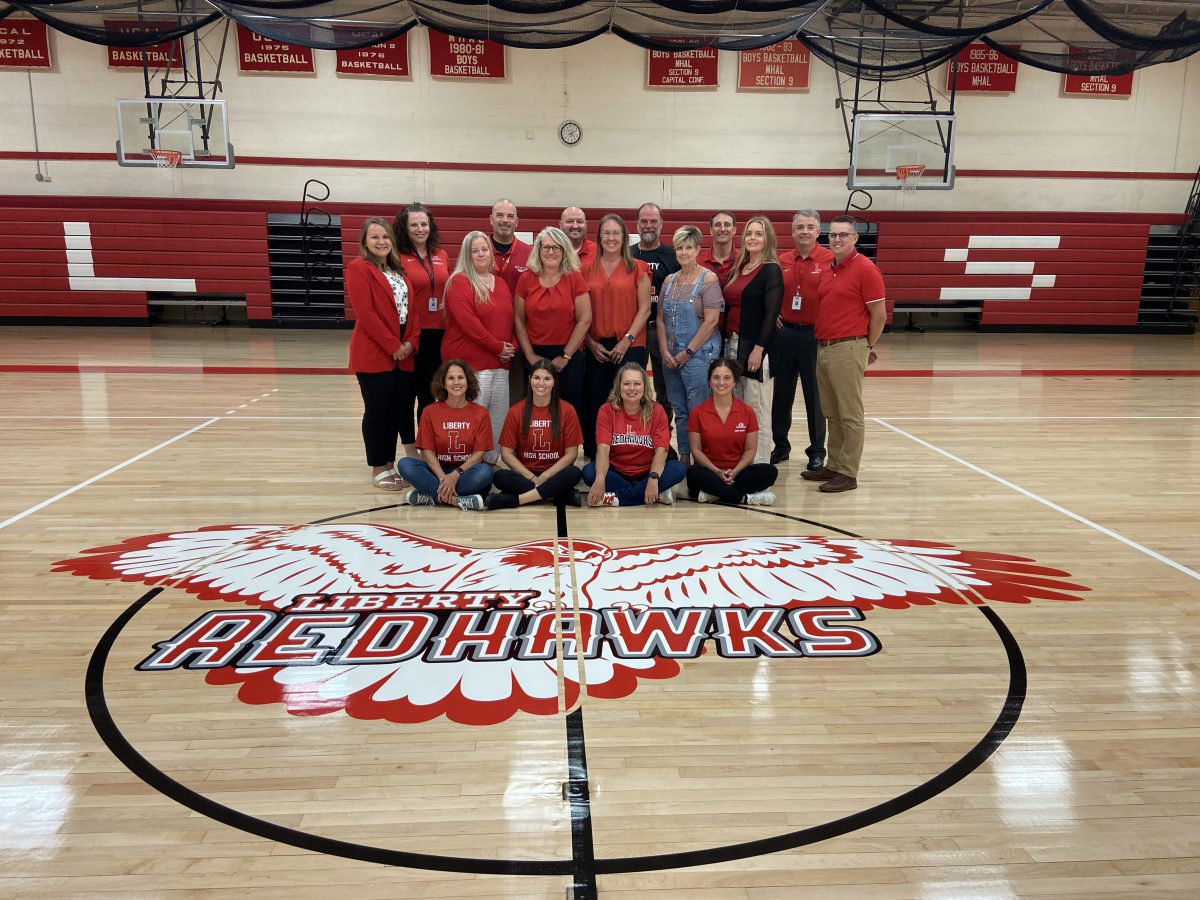 A group of administrators pose near the Redhawk logo on the gym floor.