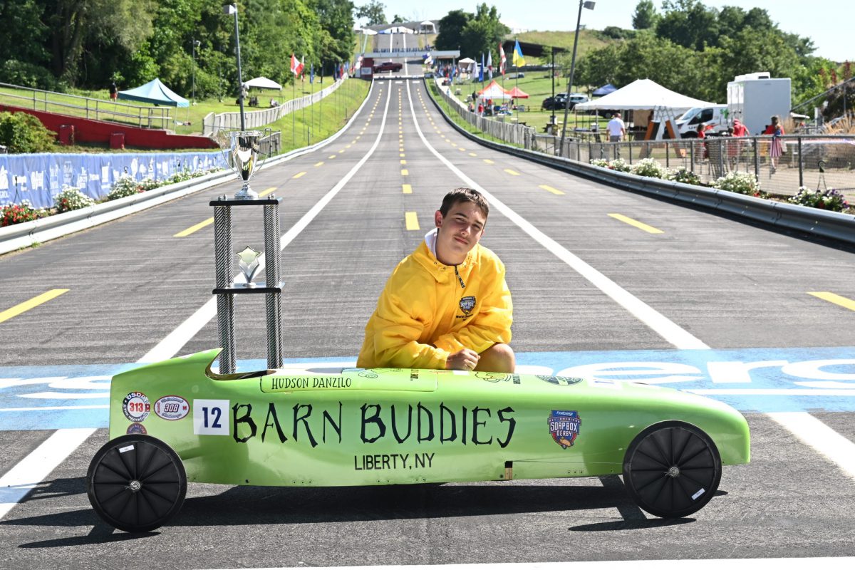 a student poses with his lime green soap box care with "Barn Buddies" on the side and a championship trophy on top of it.