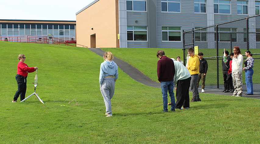 A teacher speaks near air pressure rocket launcher as students listen