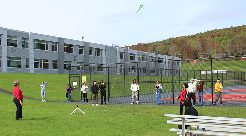 Students watch a water/airpressure rocket in the air behind the school near tennis courts