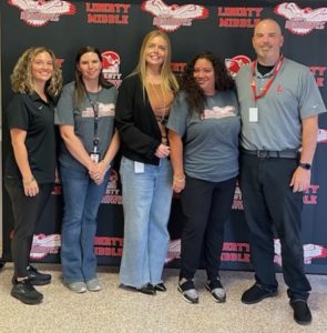 Five people stand in front of a Liberty Middle School backdrop