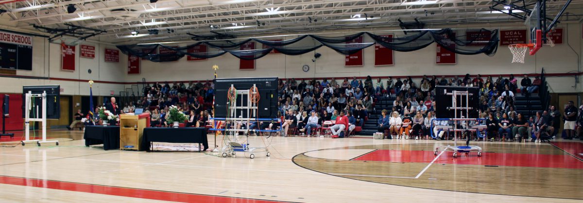 A man talks before a crowd in a gymnasium