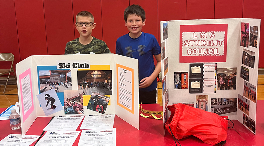 Two students sand behind display boards promoting ski club and student council