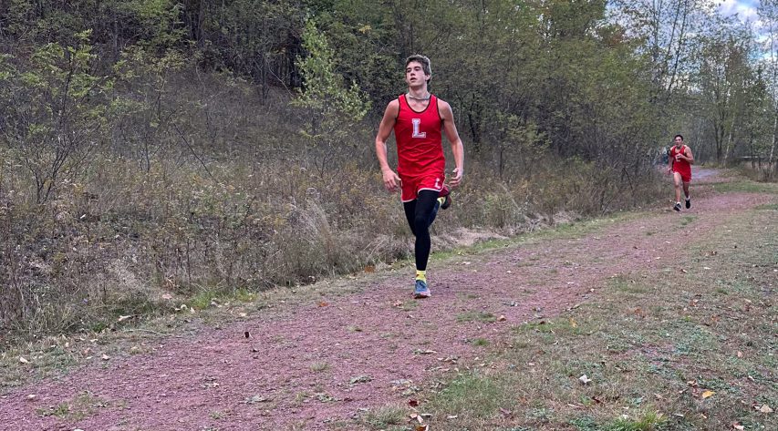 Two Liberty cross country athletes run along a path