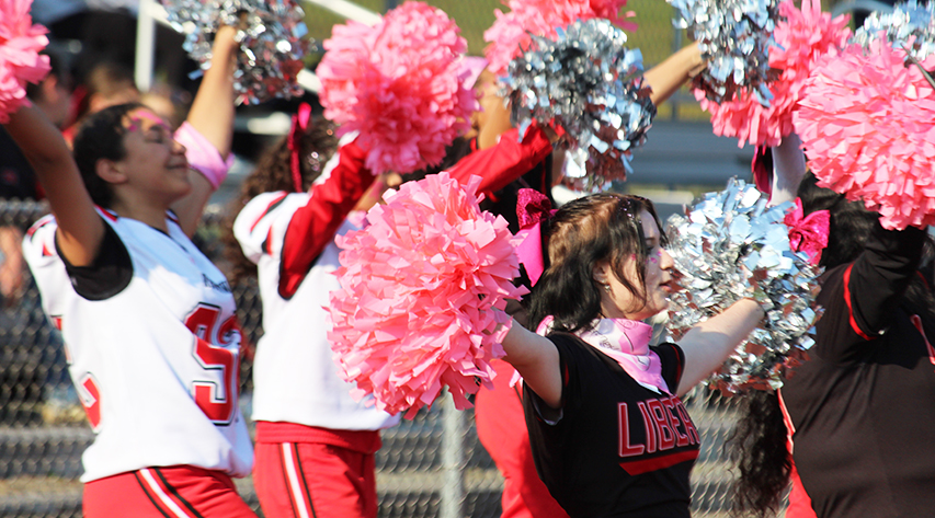 Cheer leaders in football jerseys and and black shirts wave pink and silver pompoms