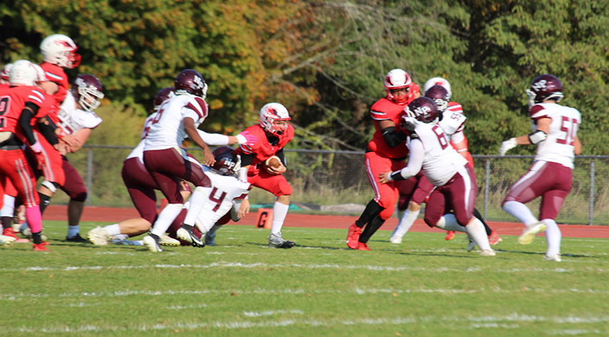 A football player carries the ball as his teammates block and the other team attempts to tackle.