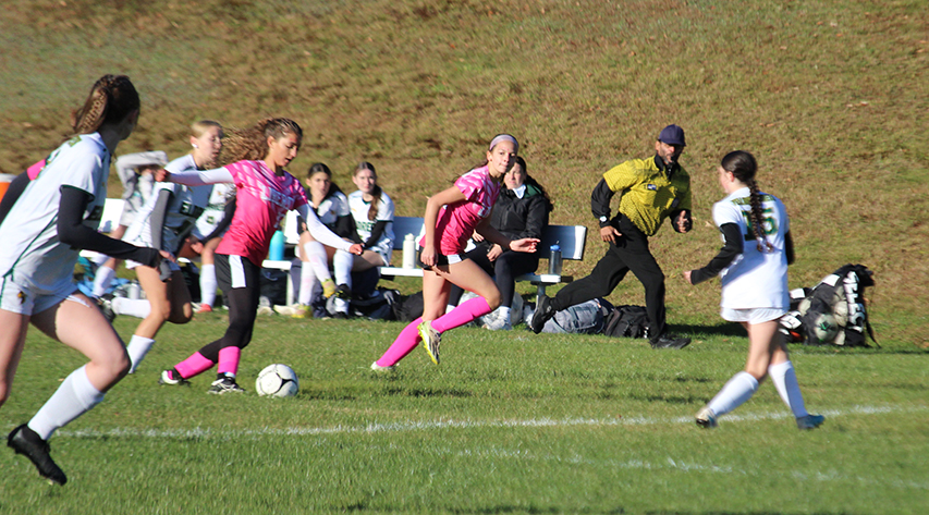 A soccer player in pink moves the ball up the field as her teammates advance with her and opponents look to defend.