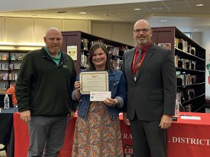 A woman holding a certificate and a piece of paper stands between two men