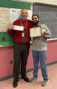 Two men pose together one holding a piece of paper and the other a certificate.