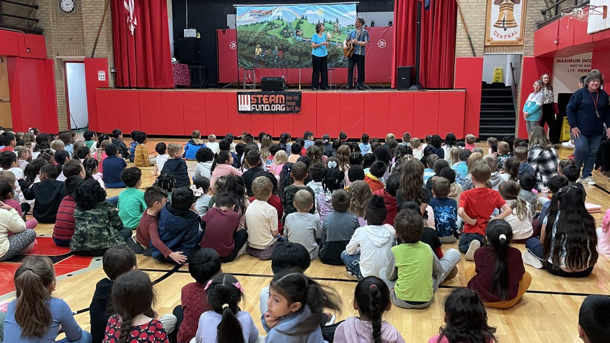 Students watch two people on the auditorium stage.