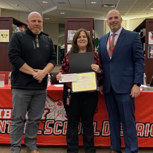 A woman holding a certificate stands between two men while posing for a photo.