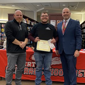 A man holding a certificate stands between two men while posing for a photo.