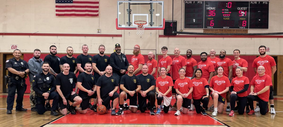 LPD team members in black shirts and LCSD team members in red shirts pose for a photo on the basketball court.