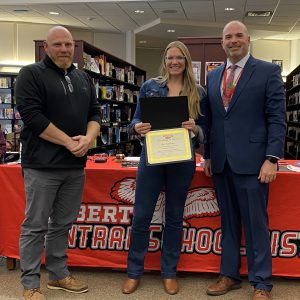 A woman holding a certificate stands between to men while posing for a photo.