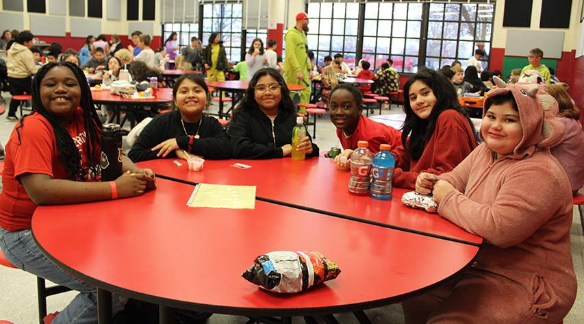 Six students smile for the camera while seated at a round table.