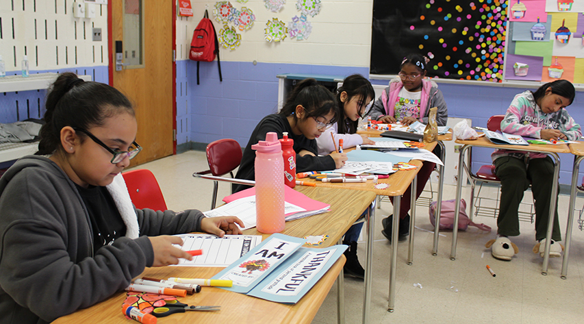 Five students work on worksheets while seated at desks