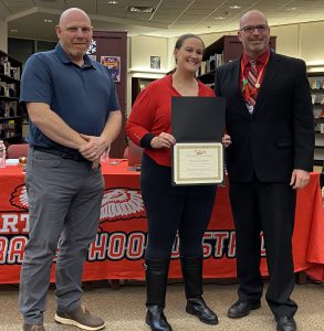 A woman holds a certificate flanked by two men.