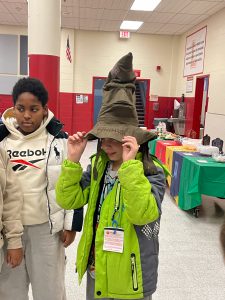 A student tries on a sorting hat as another student watches