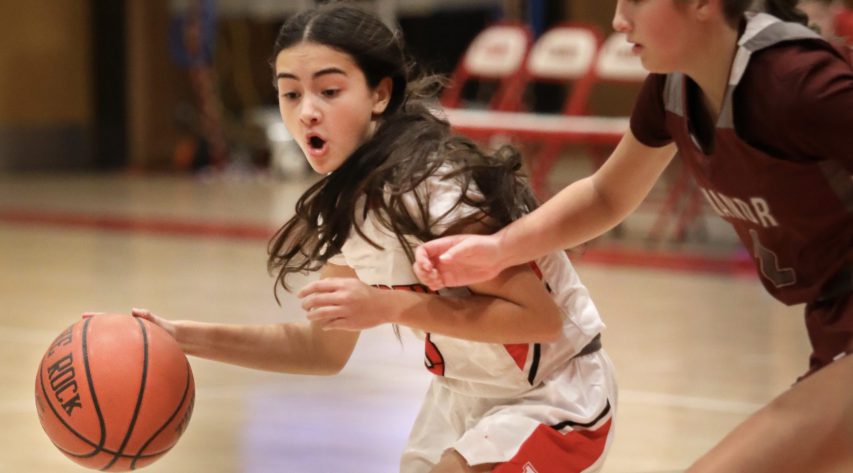 A basketball player dribbles the ball as she works around a defender