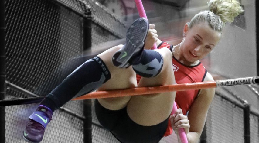 A pole vaulter touches the bar as she looks to clear