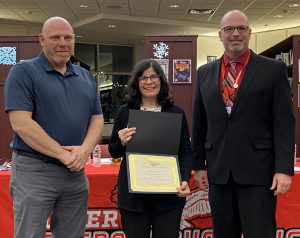 A woman holds a certificate flanked by two men.