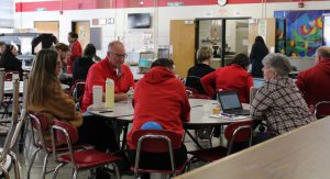 People talk while seated around round tables in the cafeteria