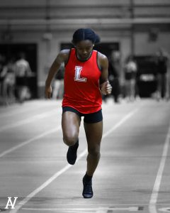 A student in a red shirt with a white L runs down the track