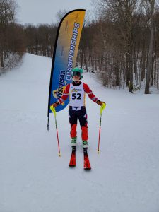 A skier stands next to a state championship flag